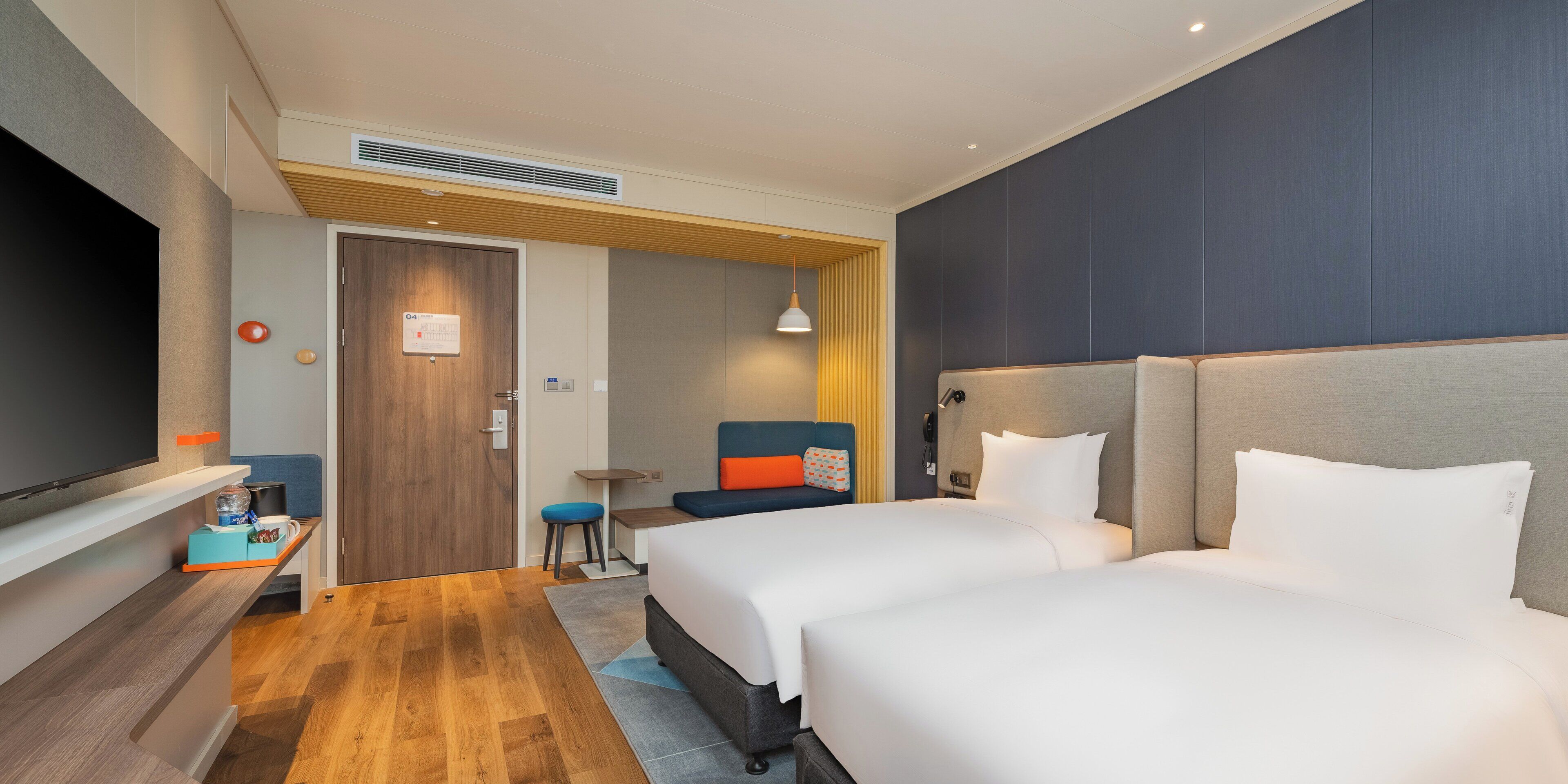 A hotel room with two beds, a desk, a television, and a door with a sign.