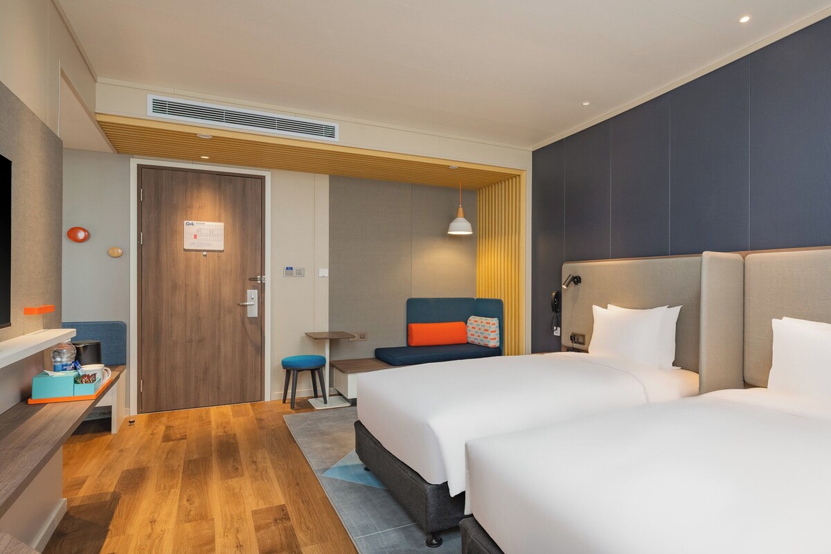 A hotel room with two beds, a TV, a desk, and a small seating area.