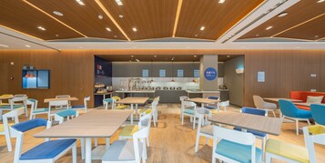 Un comedor moderno con mesas y sillas de madera, una cocina al fondo y un letrero que indica un restaurante.