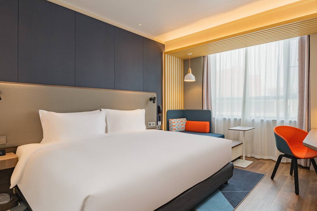 A modern hotel room with a large bed, a desk, a chair, and a TV.