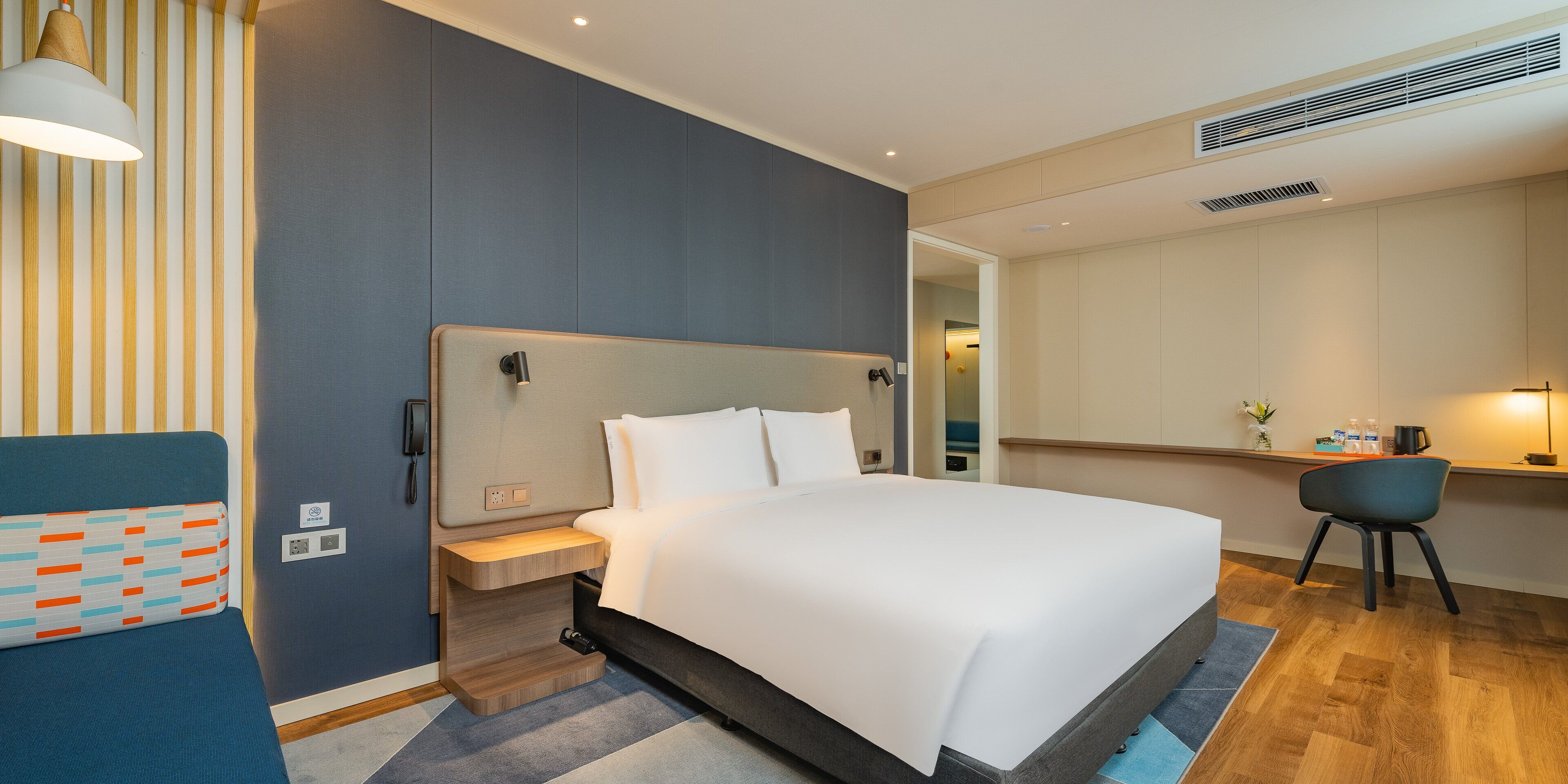 A modern hotel room with a large bed, a desk with a chair, and a small seating area.