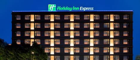 A multi-story Holiday Inn Express building with illuminated windows and a prominent green logo.