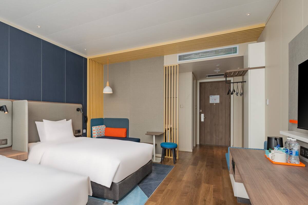 A hotel room with two beds, a desk, a TV, and a bathroom visible through an open door.
