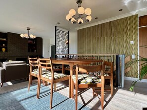 A dining area with a wooden table and chairs, a patterned wall, and a modern chandelier.