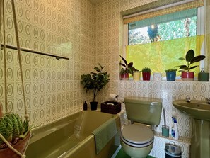 A bathroom with patterned wallpaper, a bathtub, a toilet, a sink, and several potted plants.