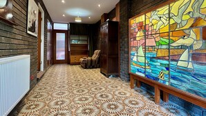 A hallway with patterned flooring, a wooden chair, a bookshelf, and a stained glass window depicting birds. - Pant Golau House (Llanbedr)