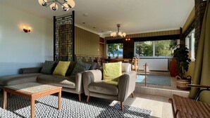 A living room with a sofa, armchairs, a coffee table, patterned rug, and a decorative wall panel. - Pant Golau House (Llanbedr)