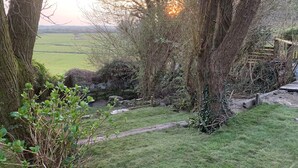 A garden with a stone wall, a wooden fence, and a view of a green field. - Pant Golau House (Llanbedr)