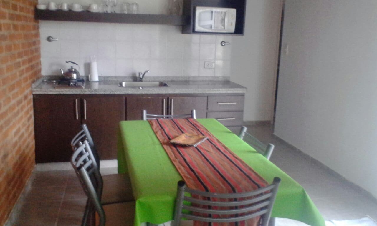 Una cocina compacta con zona de comedor, que incluye una mesa verde, sillas y un camino de mesa a rayas.