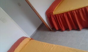 A room with two beds, each with a red and yellow bedspread. The room has a tiled floor and white walls. - Complejo La Loma (Federacion)