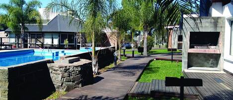 Una piscina con un muro de piedra, un muelle de madera y una zona verde con un banco.