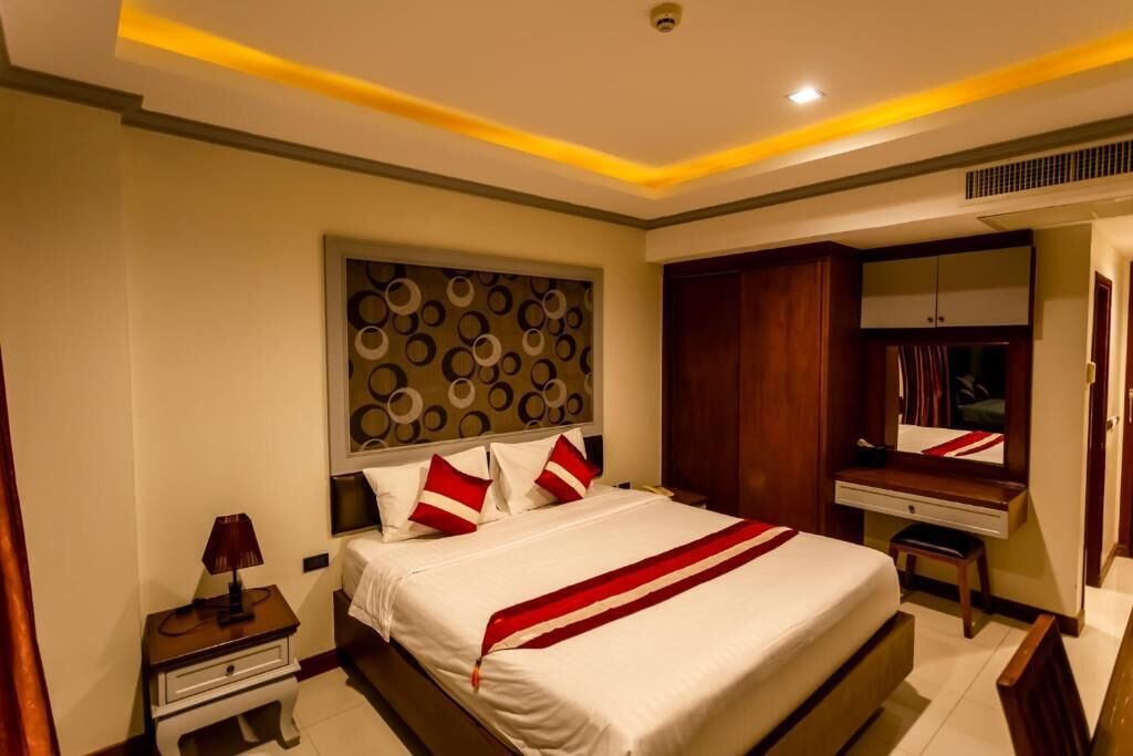 A hotel room with a large bed, a bedside table with a lamp, a wardrobe, and a mirror.