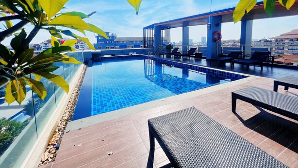 Piscina infinita en la azotea con sillones de descanso y barandilla de cristal.