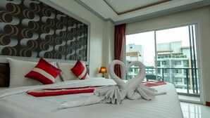 Habitación de hotel con una cama grande, un cabecero con diseño circular, vistas de edificios a través de un ventanal amplio y una presentación de toallas con forma de cisne en la cama.