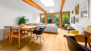 Un salon moderne avec une table à manger en bois, des chaises, un canapé et une grande fenêtre donnant sur un paysage verdoyant.