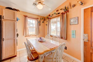 Uma sala de jantar com uma mesa de madeira, cadeiras brancas e um ventilador de teto.