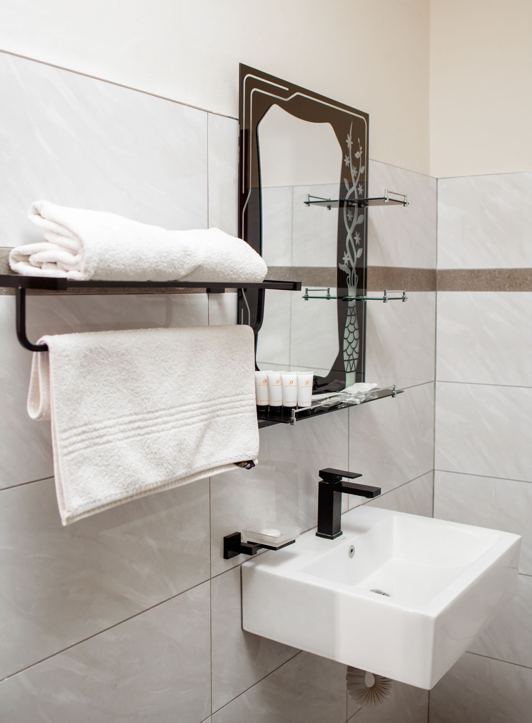A bathroom with a white sink, a towel rack with folded towels, a mirror with a decorative frame, and toiletries on a shelf.