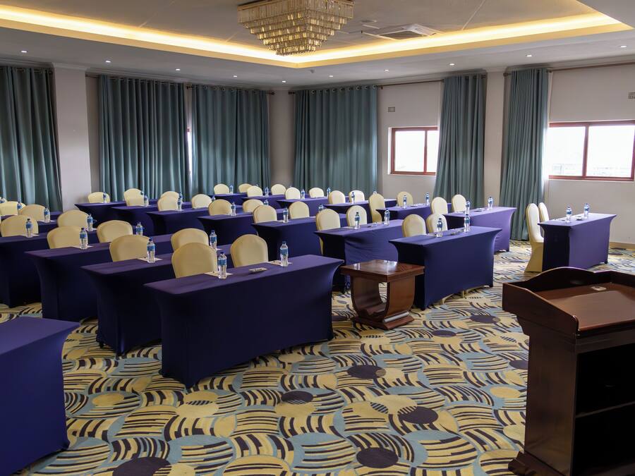 A conference room with rows of tables and chairs, a podium, and a patterned carpet.