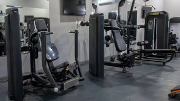 A gym with various exercise machines, a TV mounted on the wall, and a mirror reflecting the equipment.