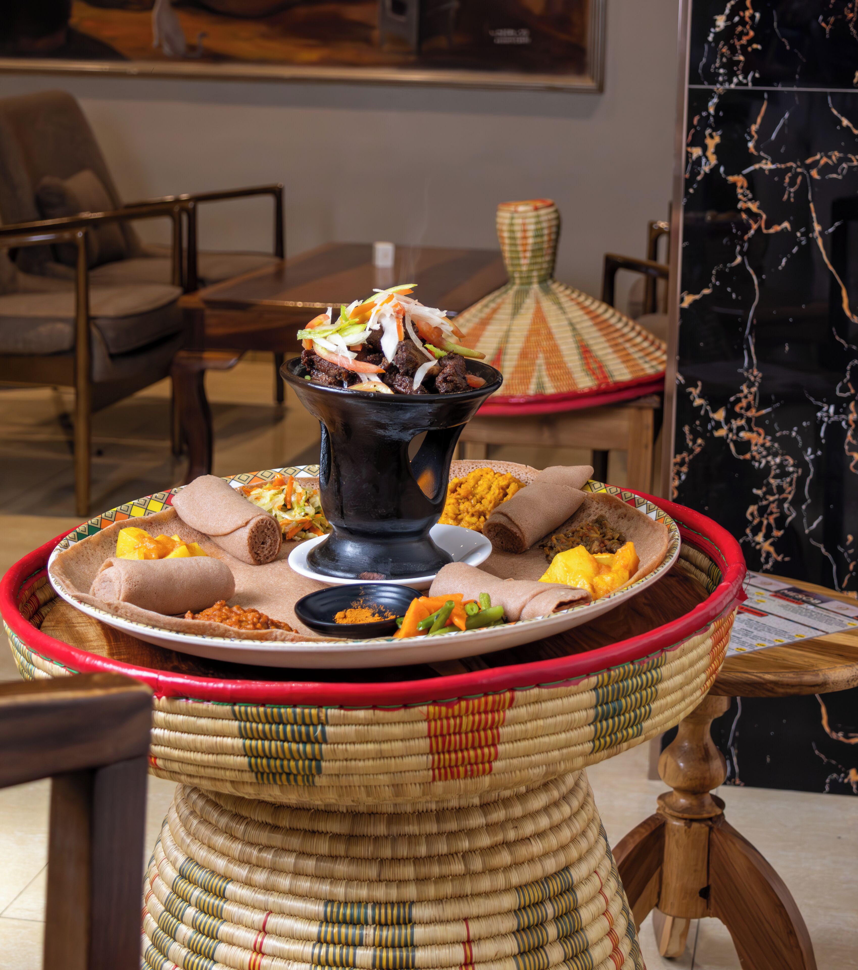Una comida tradicional etíope con injera, varios guisos y una olla negra grande.