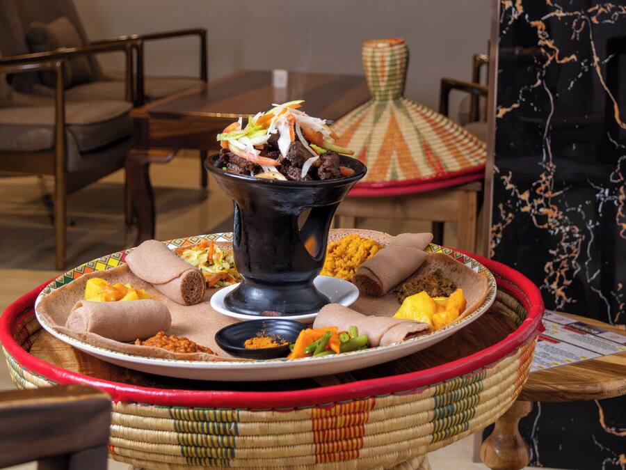 Presentació tradicional d'un àpat etíop, amb injera, diferents estofs i una olla negra gran.