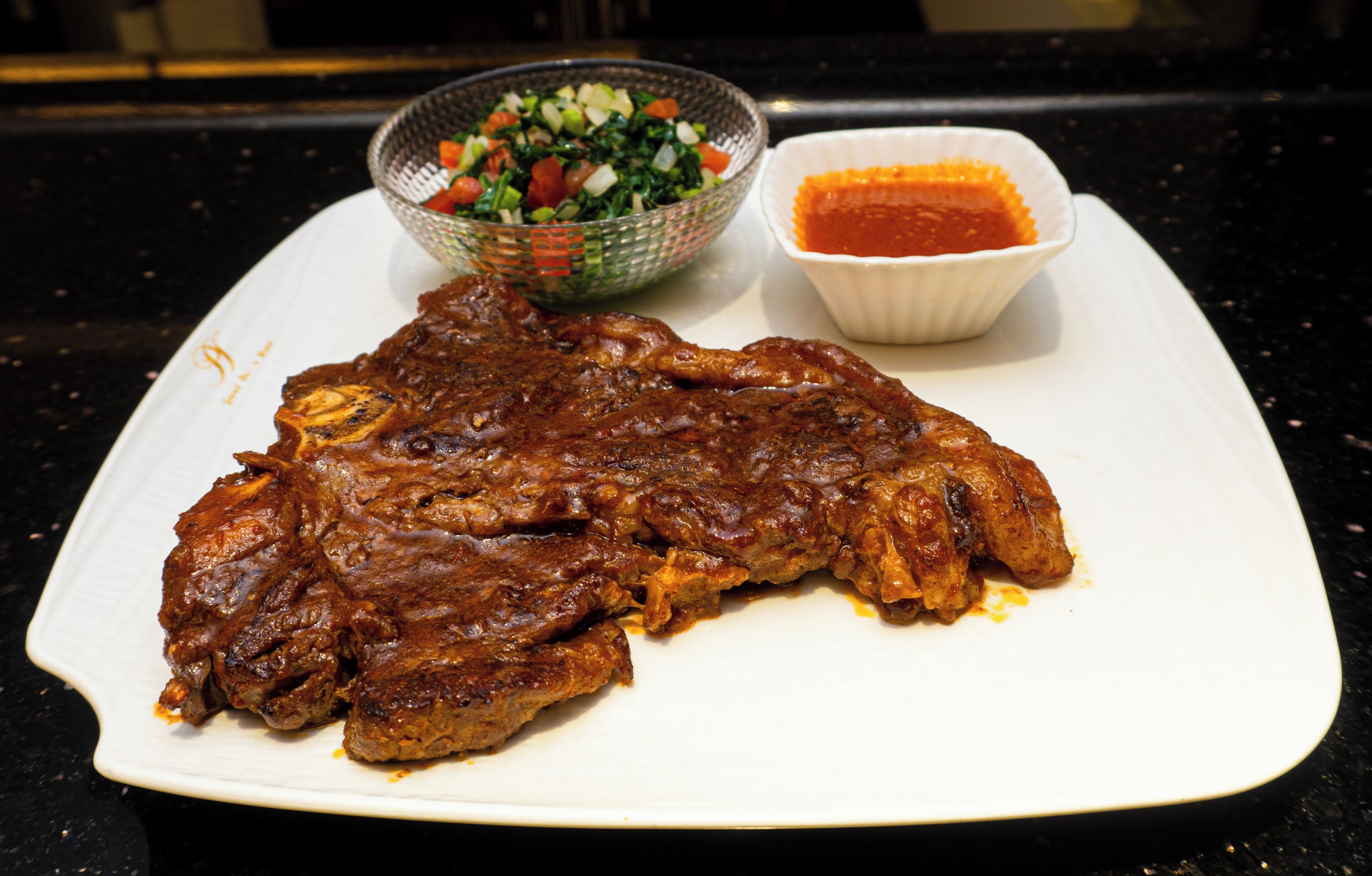 A plate with grilled meat and a side of salad and sauce.