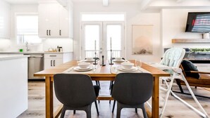 Una cocina moderna con armarios blancos, una mesa de comedor de madera dispuesta para dos personas y una trona para bebé.
