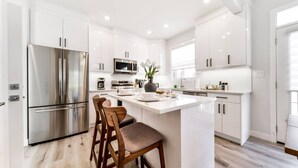 Una cocina moderna con armarios blancos, electrodomésticos de acero inoxidable y una isla central con asientos.