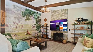 A living room with a mural of deer, a fireplace, and a TV displaying streaming services. - Disney Explorer - Sauna, Theater, Arcade and More! (Garden Grove)