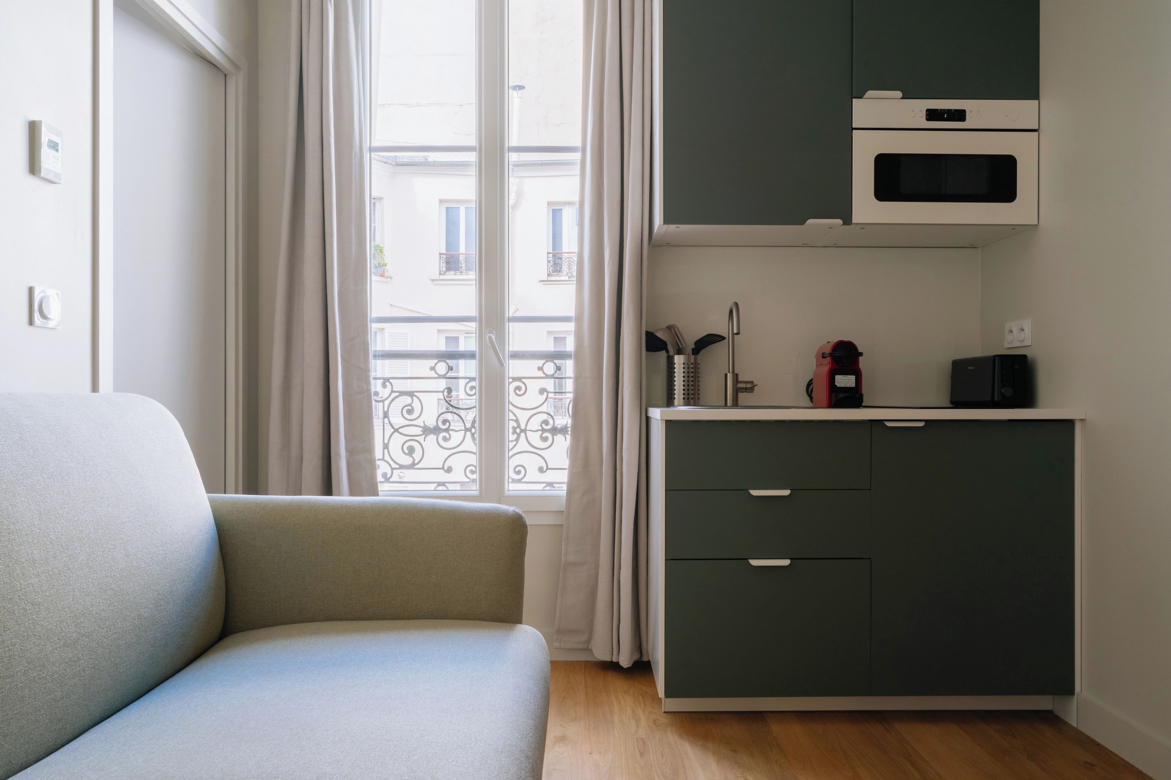 Ein Zimmer mit einer Couch, einer Küchenzeile mit Mikrowelle und Blick ins Freie.