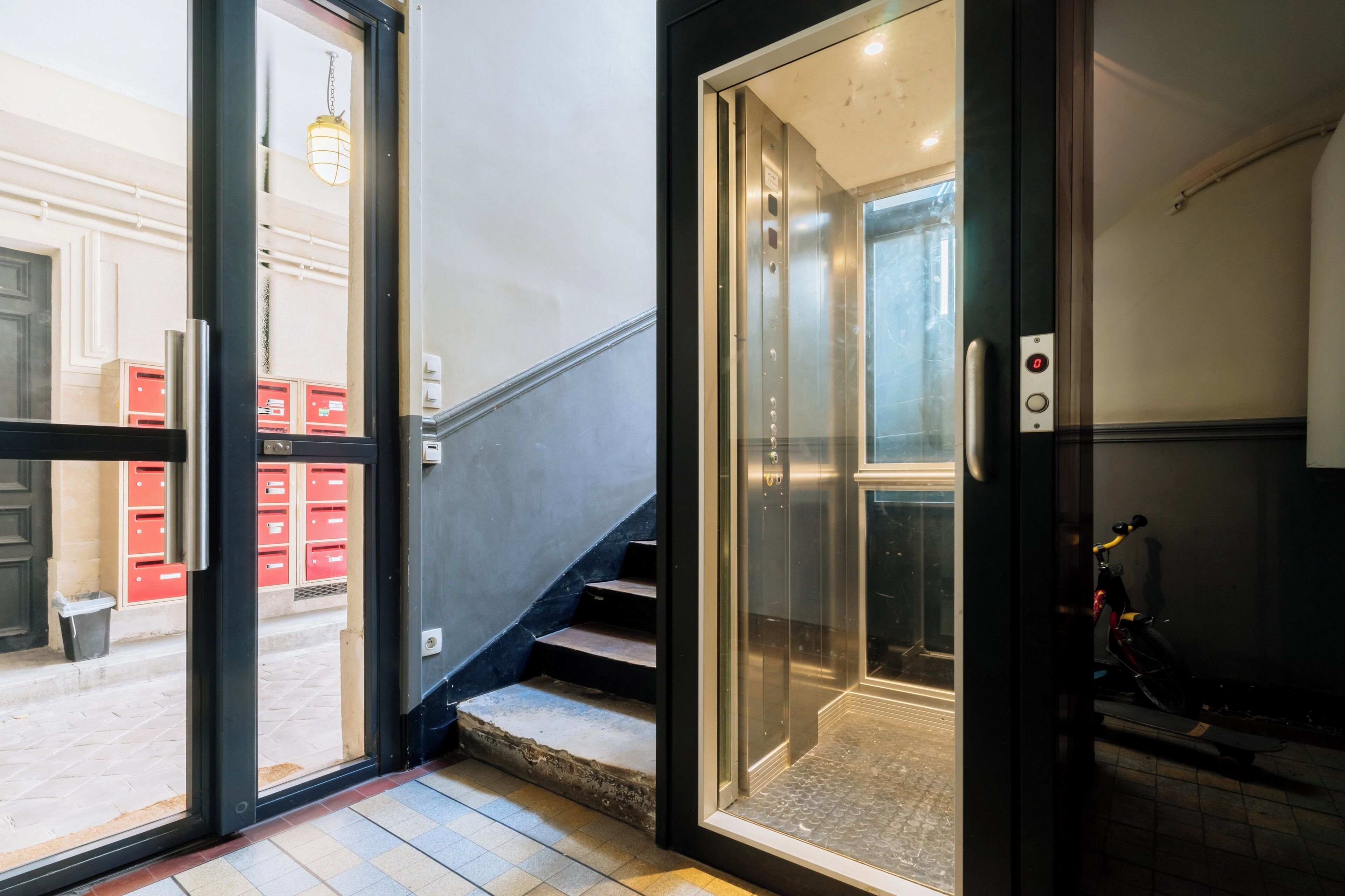 An interior view of a building with a staircase leading to an elevator, a door leading outside, and a bicycle parked inside.