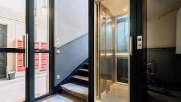 An interior view of a building with a staircase leading to an elevator, a door leading outside, and a bicycle parked inside.