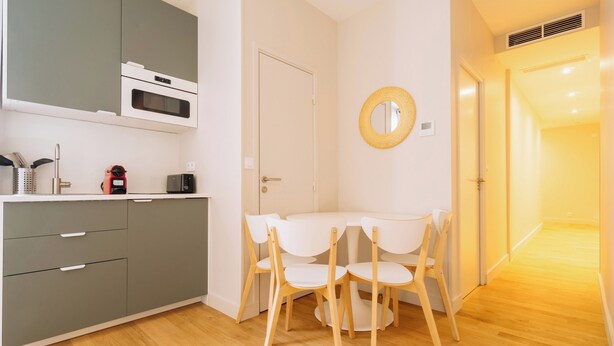 Moderni keittiö, jossa on harmaat kaapit, mikroaaltouuni sekä ruokailutila, jossa on pieni pöytä ja neljä tuolia.