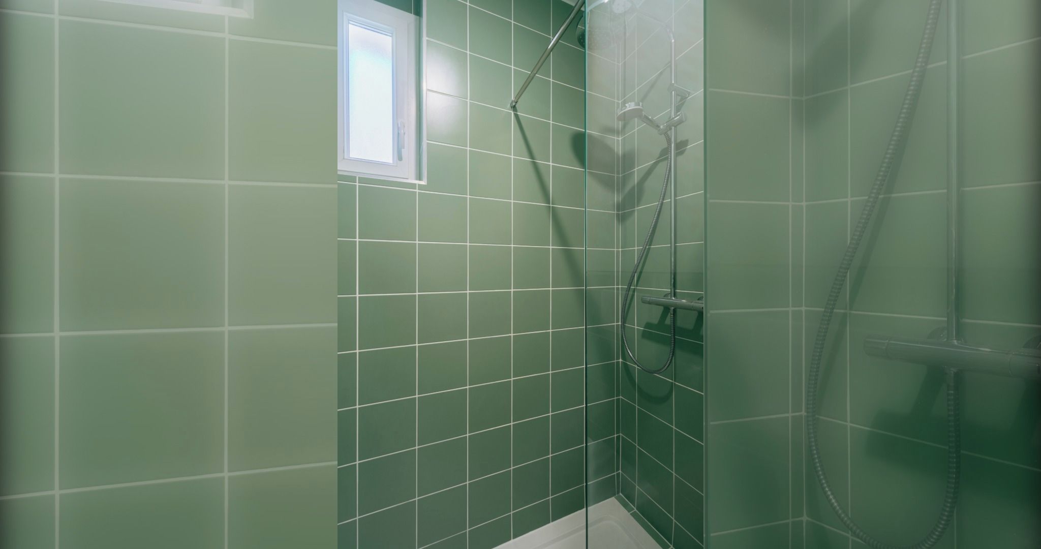A bathroom with green tiles, a shower, and a window.