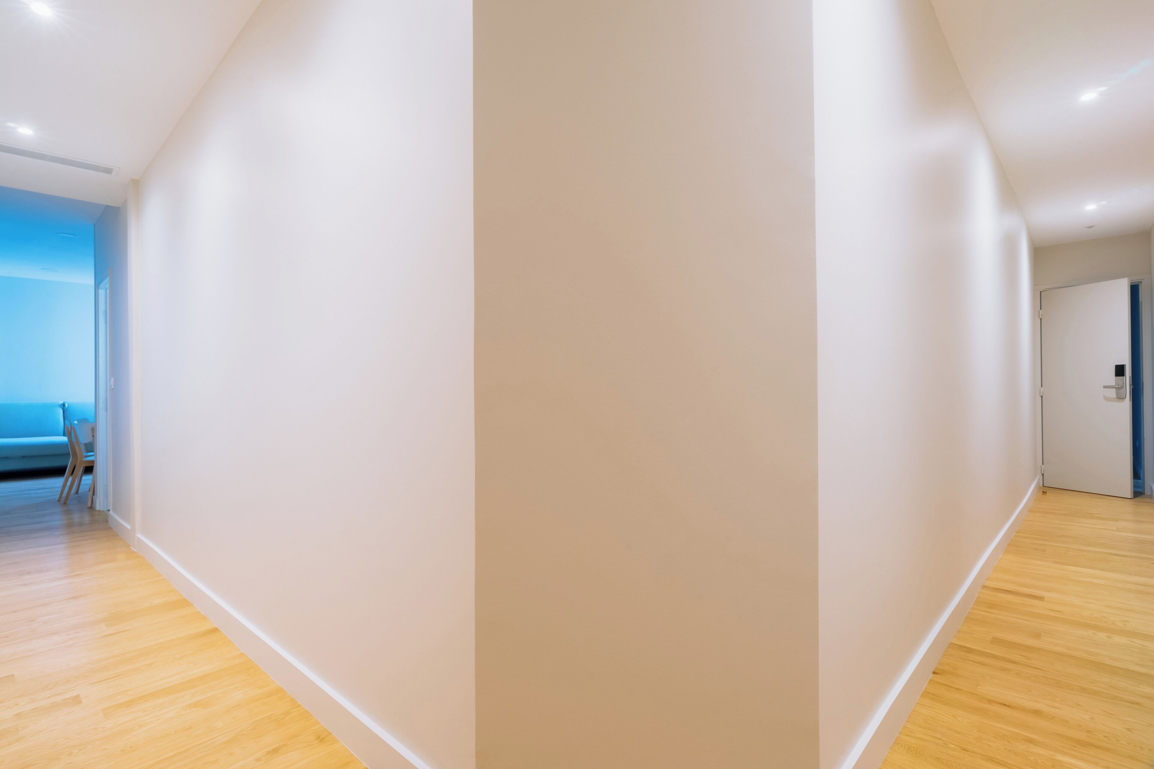 Un couloir doté d’un plancher en bois, d’un mur bleu et d’une porte donnant sur une autre pièce.