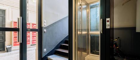 An interior view of a building with a staircase leading to an elevator, a door leading outside, and a bicycle parked inside.