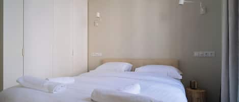 A neatly made bed with white linens and towels, a wooden nightstand with a lamp, and a wardrobe with a mirror.
