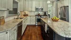 Una cocina moderna con armarios blancos, encimeras de granito, electrodomésticos de acero inoxidable e iluminación colgante.