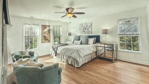 Un dormitorio con cama, ventilador de techo, mesita de noche y ventana.