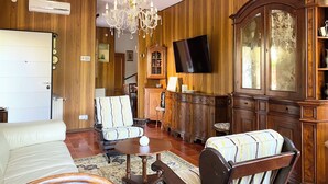 Un salon traditionnel avec des boiseries, un lustre, un téléviseur et un meuble avec des portes en verre.
