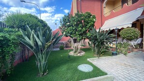Une cour avec de l’herbe verte, diverses plantes, un petit arbre et un bâtiment à la façade rouge.