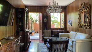 Un salon avec des boiseries, un lustre, un canapé, une table basse, un téléviseur et un coin repas comprenant des chaises et une table.