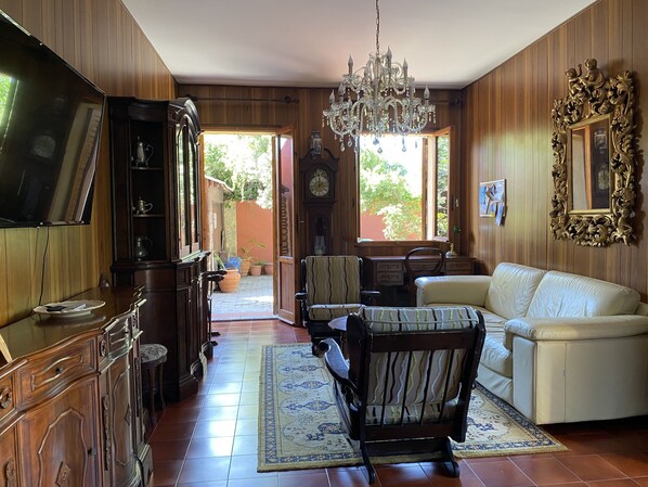 Ein Wohnzimmer mit Holzvertäfelung, einer Chandelier, einer Couch, einem Couchtisch, einem Fernseher und einem Essbereich mit Stühlen und einem Tisch.