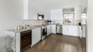 A modern kitchen with white cabinetry, a marble countertop, stainless steel appliances, and a wooden floor.