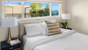 A neatly made bed with white linens, a striped pillow, and two bedside lamps. There is a small bedside table with a book and a lamp.