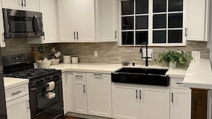 A modern kitchen with white cabinets, a black stove, a microwave, and a window above the sink.
