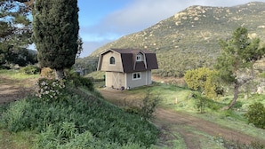 A small house with a sloped roof, surrounded by a natural landscape with a mountain in the background.
