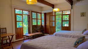 A cozy room with two beds, large windows, a stone fireplace, and wooden beams.