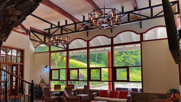 A spacious lounge area with large windows, wicker furniture, and a staircase leading to an upper level.