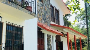 A two-story house with a stone facade, a red-tiled roof, and a covered porch with red pillars.